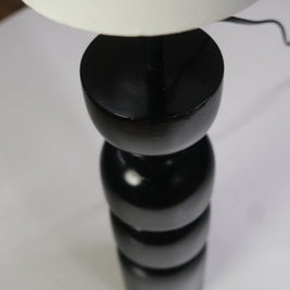 Contemporary table lamp featuring a glossy black geometric base and a white cylindrical lampshade on a desk.