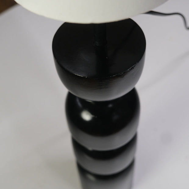 Contemporary table lamp featuring a glossy black geometric base and a white cylindrical lampshade on a desk.