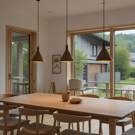 Dining area with wooden table and chairs in a room with large windows showing a view of a house and trees.