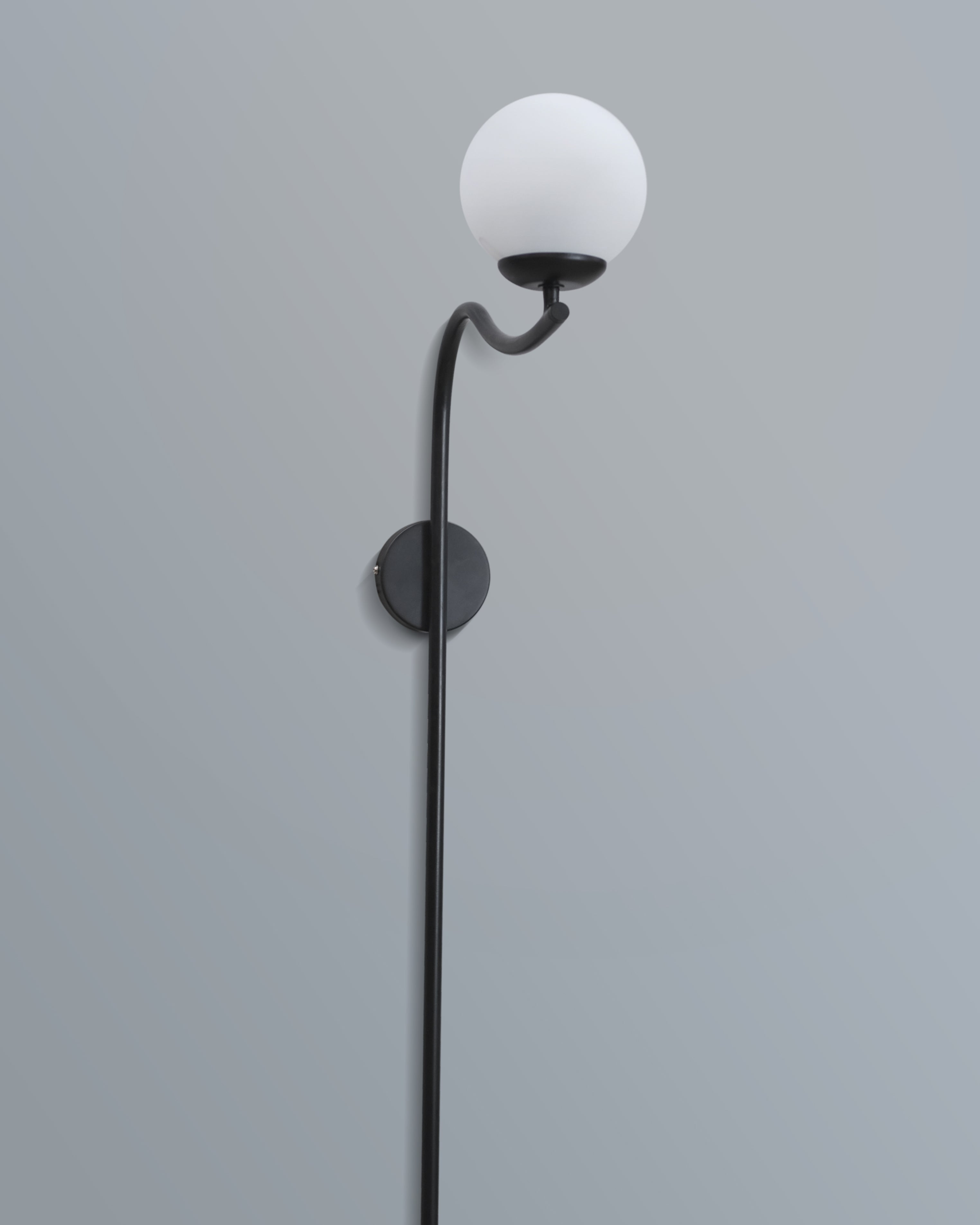 Elegant arched wall lamp featuring a black metal frame and a soft-glow white lampshade, enhancing a stylish interior.