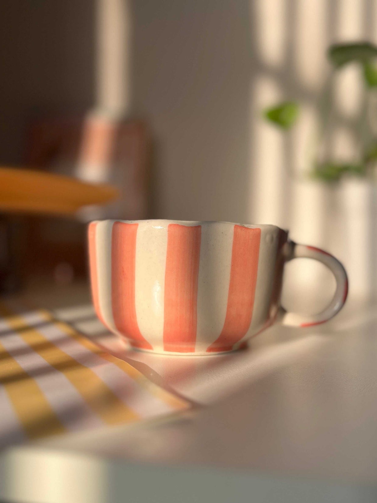 Striped peach ceramic cup on a table with a blurred background