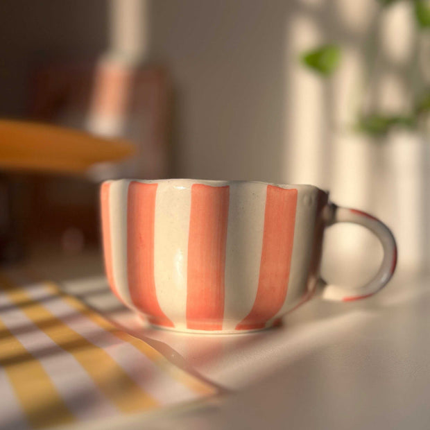 Striped peach ceramic cup on a table with a blurred background