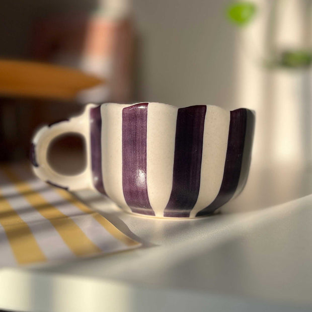 Striped ceramic cup on a table with a blurred background. purple, blackcurrant color. 