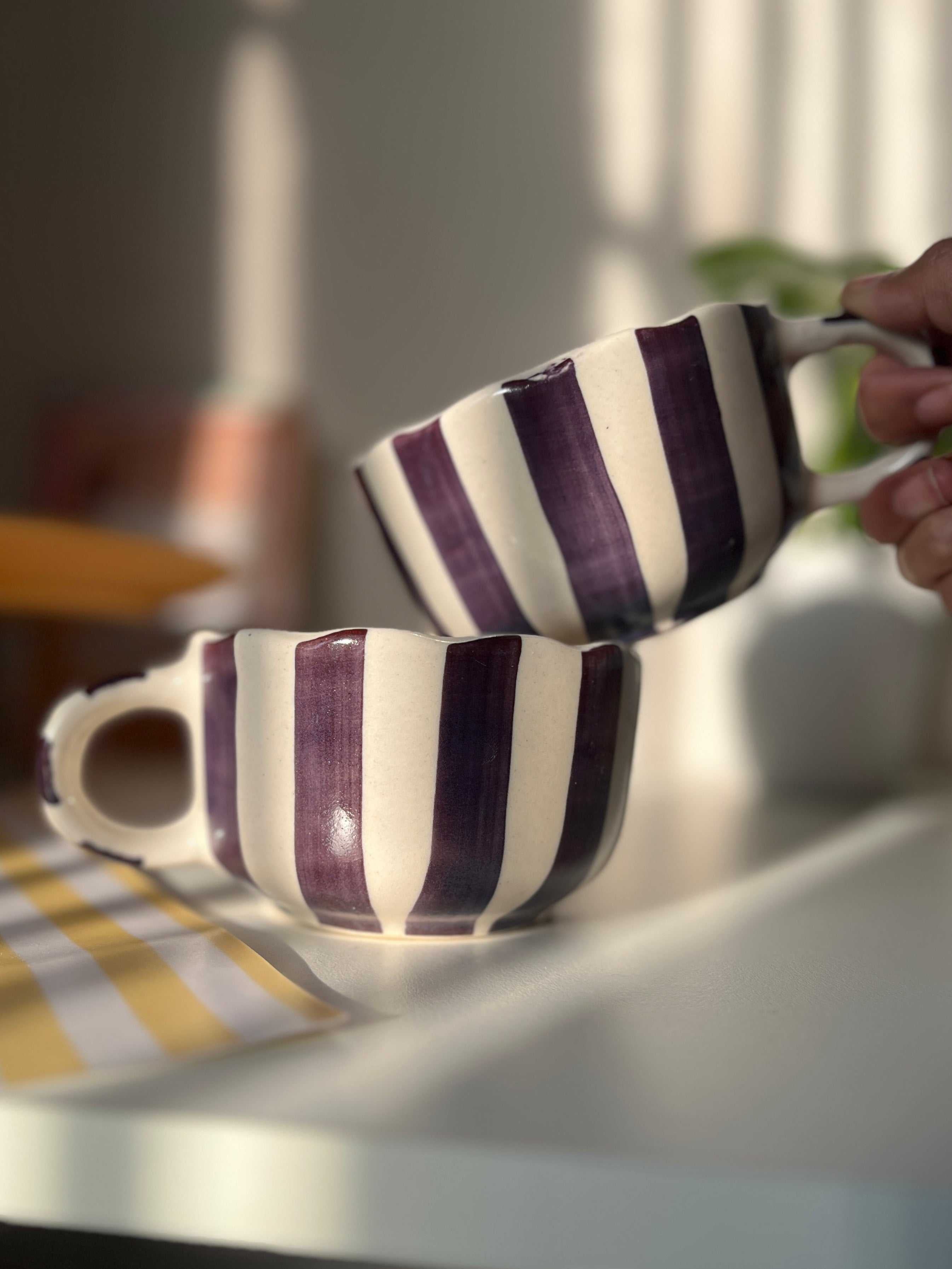 Two striped purple and white mugs on a table with a blurred background