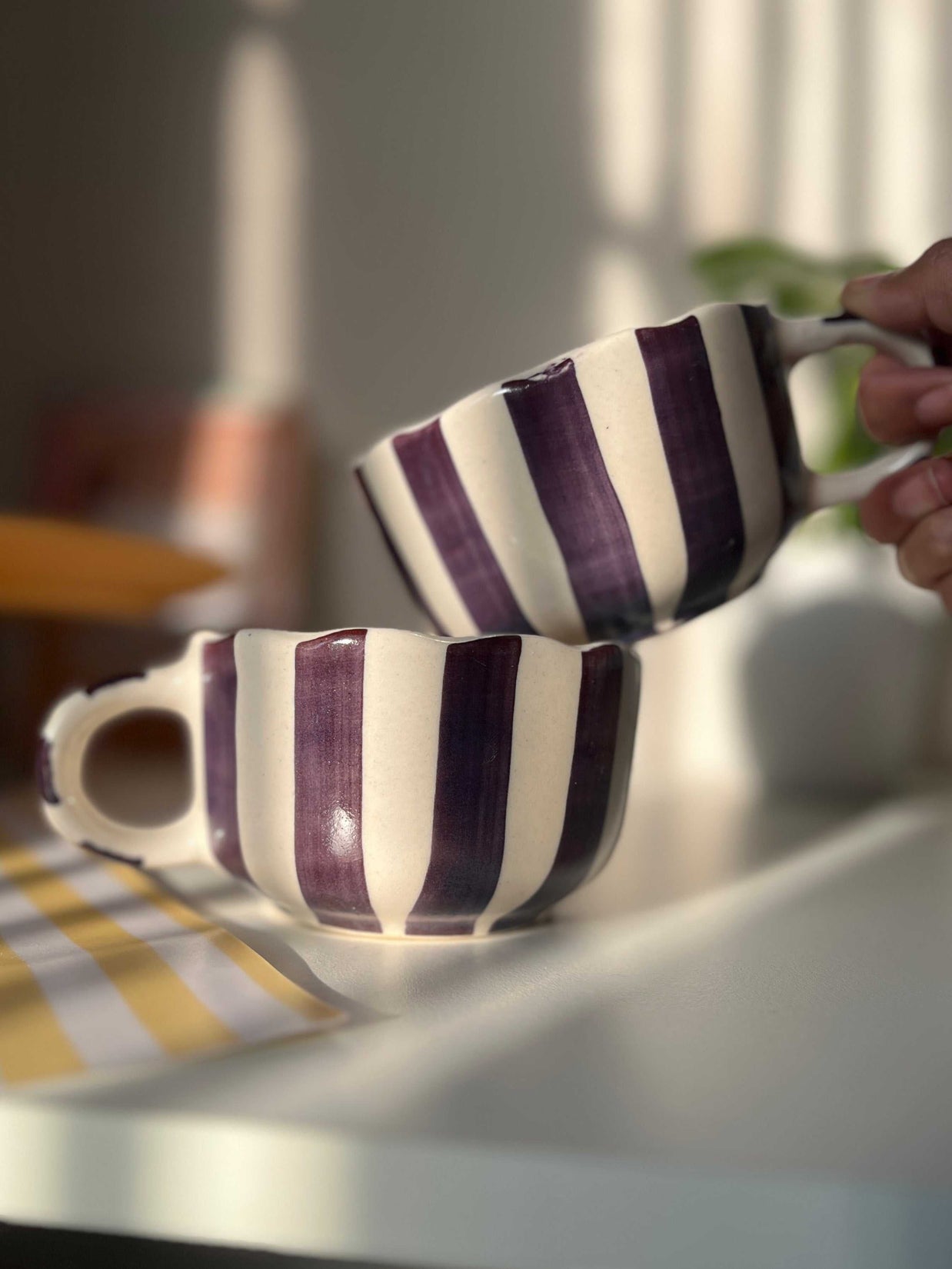 Two striped purple and white mugs on a table with a blurred background