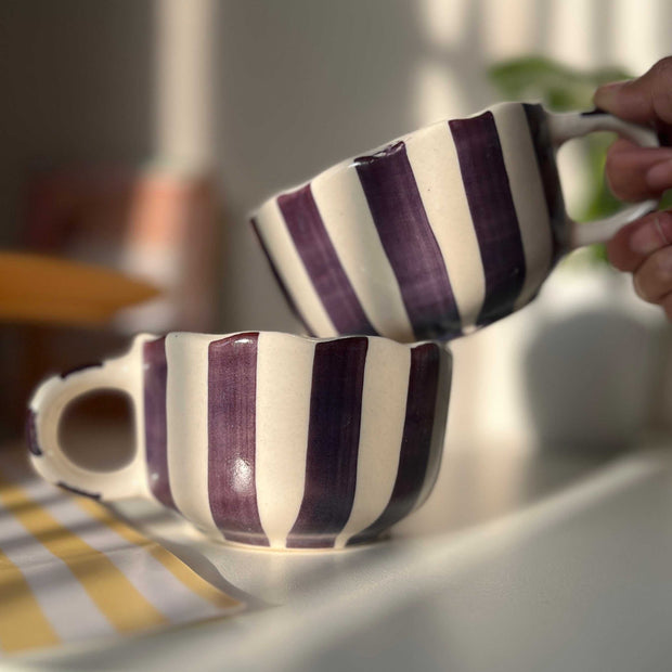 Two striped purple and white mugs on a table with a blurred background