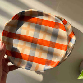 Round, checkered fabric styled plate held by a hand on a light background