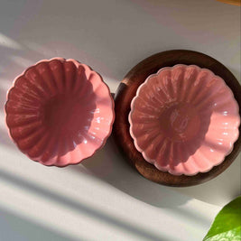 Two pink ceramic dishes on a white surface with a plant leaf in the corner.