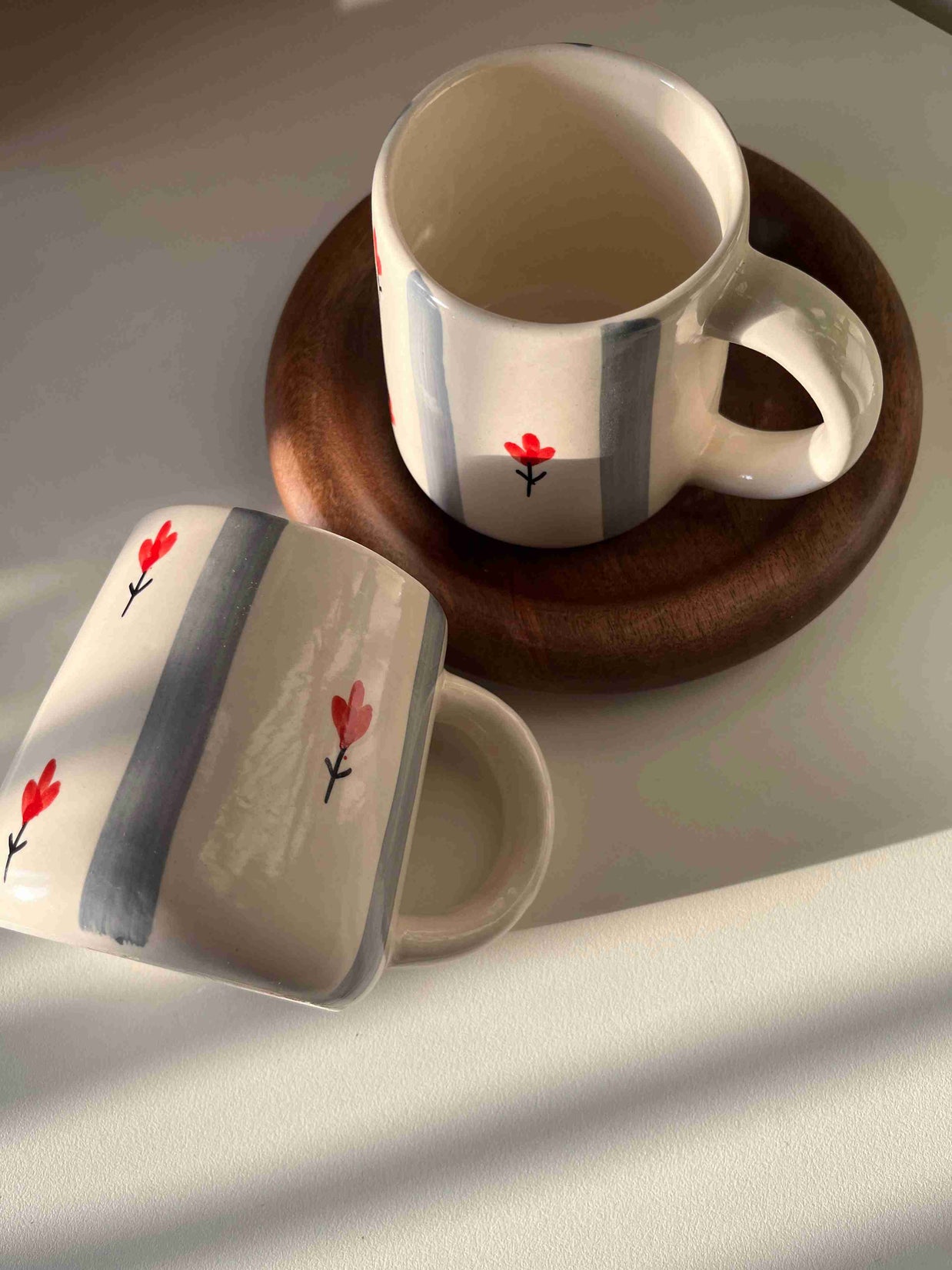 Two ceramic mugs with floral designs on a wooden coaster.