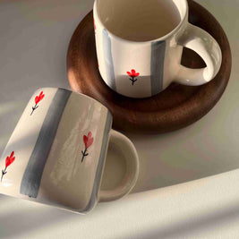 Two ceramic mugs with floral designs on a wooden coaster.