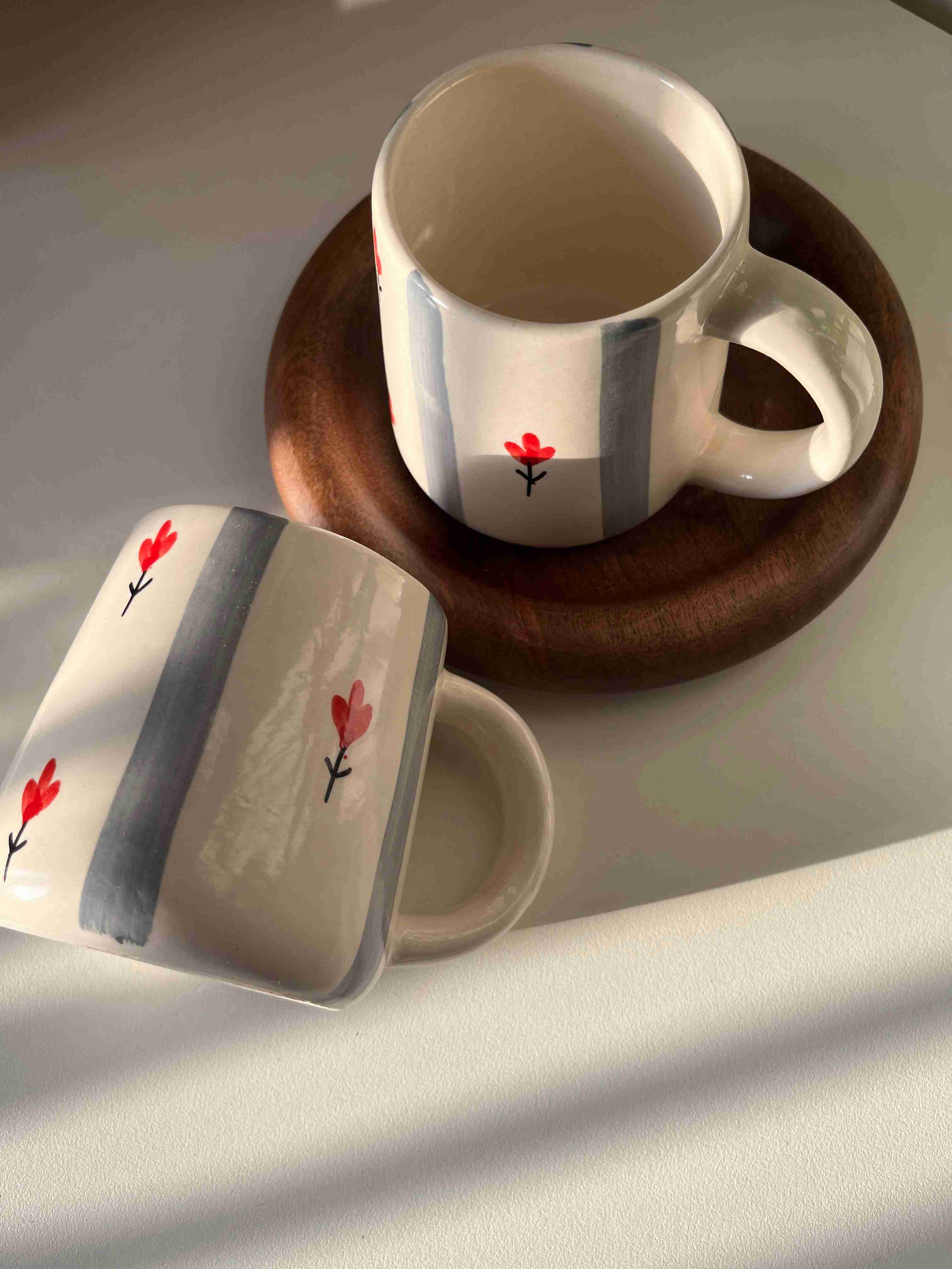 Two ceramic mugs with floral designs on a wooden coaster.