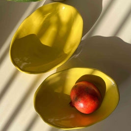 Two yellow ceramic bowls with a pomegranate on a light background