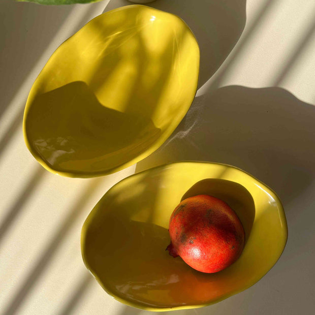 Two yellow ceramic bowls with a pomegranate on a light background