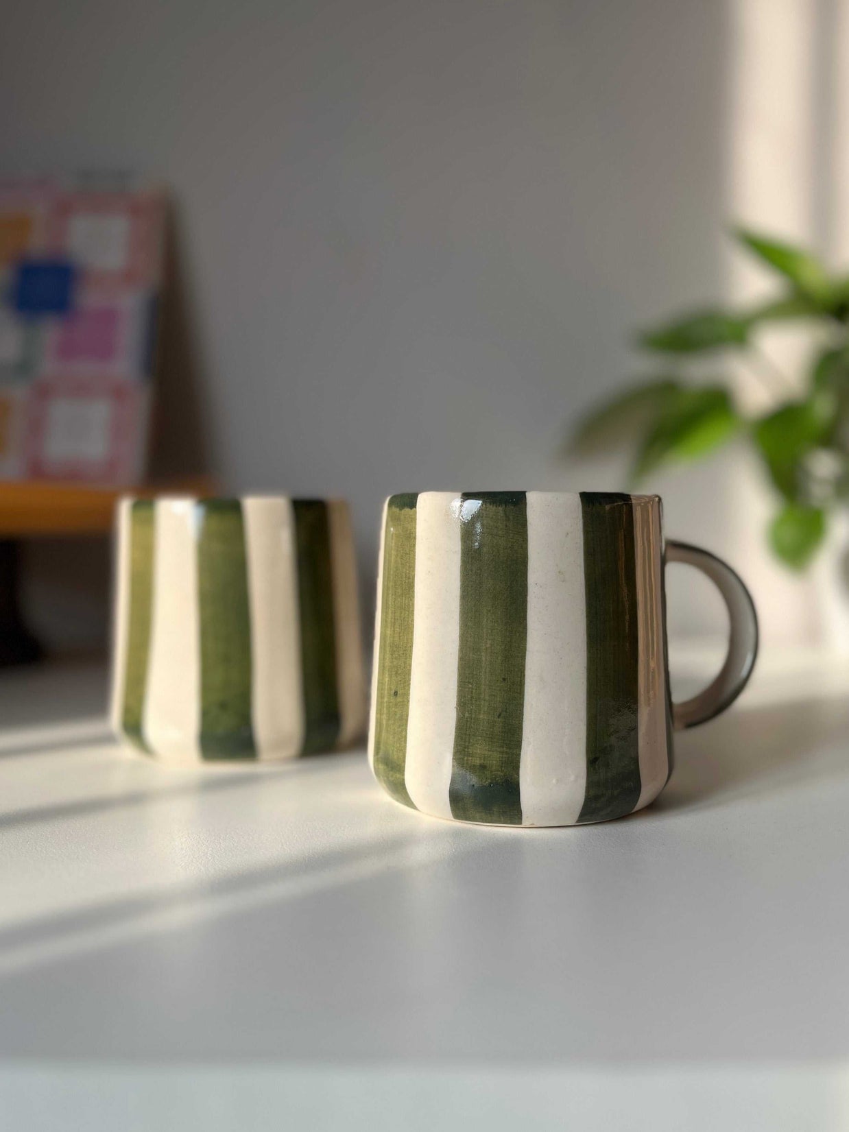 Two green ceramic coffee mugs with striped design on a light surface
