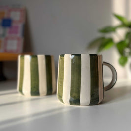 Two green ceramic coffee mugs with striped design on a light surface