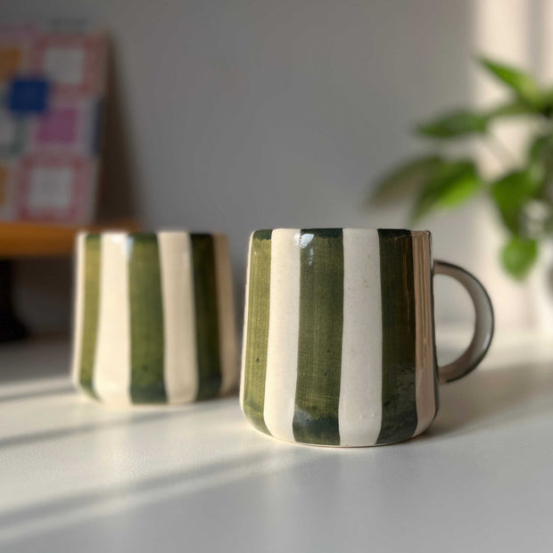 Two green ceramic coffee mugs with striped design on a light surface