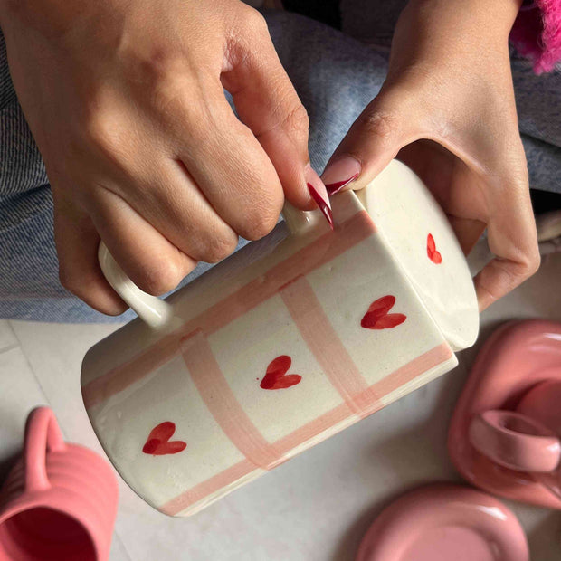 Person holding a pink mug with heart designs on a tiled floor.