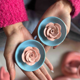 Hands holding blue incense stick holders with pink rose-shaped ceramic flower in 3D