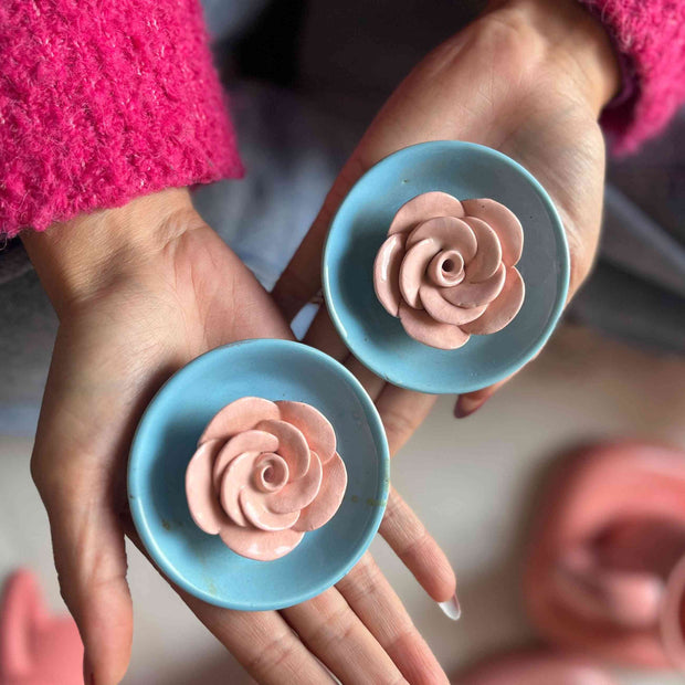 Hands holding blue incense stick holders with pink rose-shaped ceramic flower in 3D