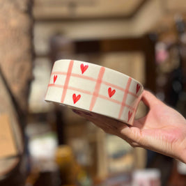 Ceramic cup with red heart pattern held by a hand in a blurred indoor setting