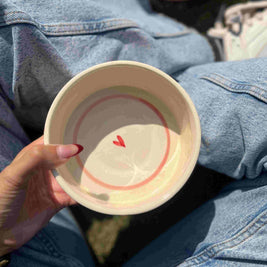 Hand holding a ceramic bowl with a red heart design on denim jeans.