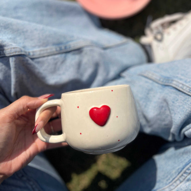 Person holding a small white container with a red heart on top, wearing a denim jacket. The heart is 3D and beautifully handcrafted.