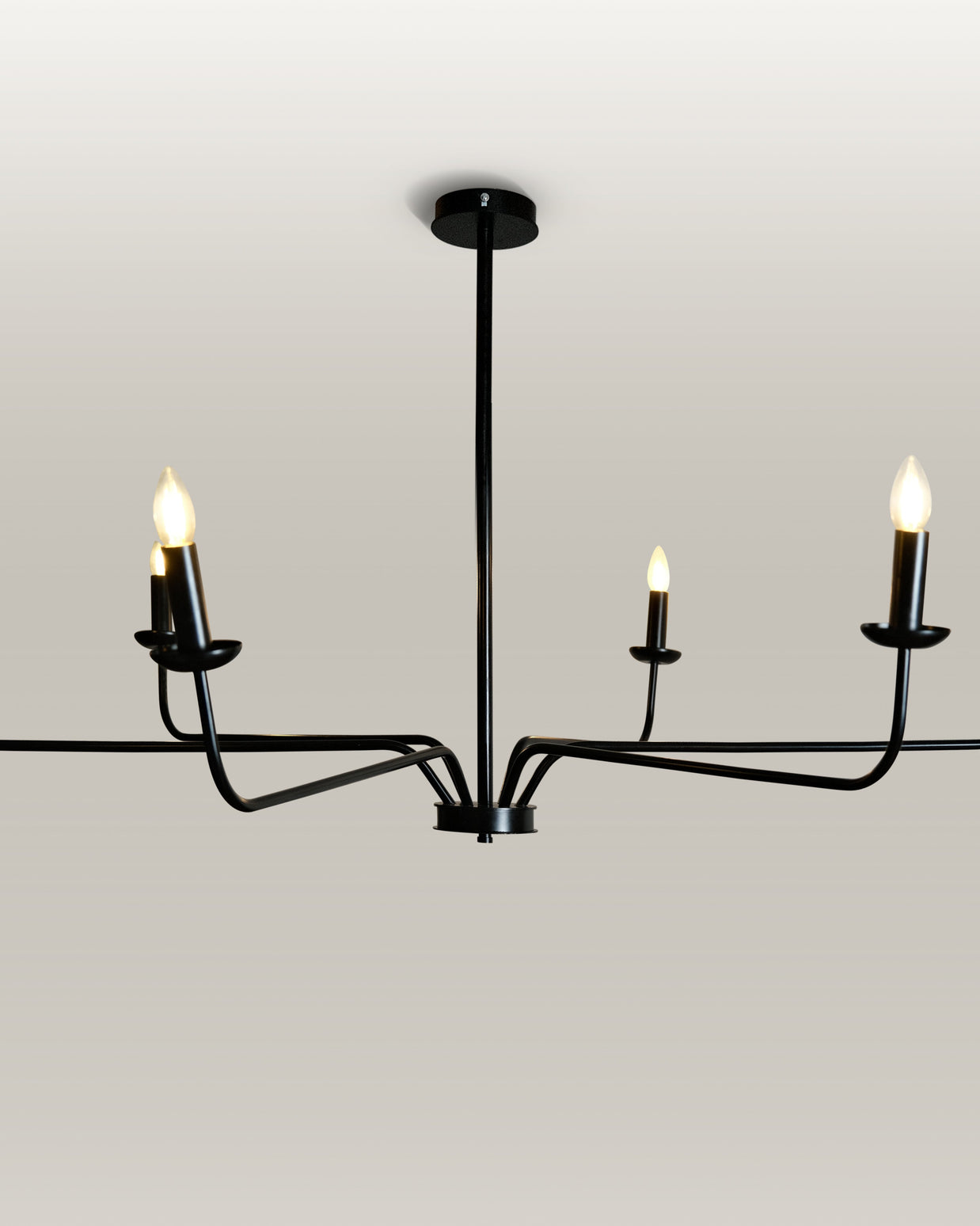 Minimalist chandelier featuring six black metal arms and candle flame light bulbs, illuminating a contemporary dining area.