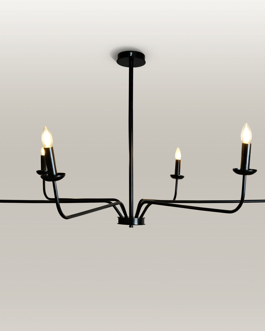 Minimalist chandelier featuring six black metal arms and candle flame light bulbs, illuminating a contemporary dining area.