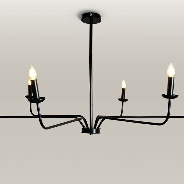 Minimalist chandelier featuring six black metal arms and candle flame light bulbs, illuminating a contemporary dining area.