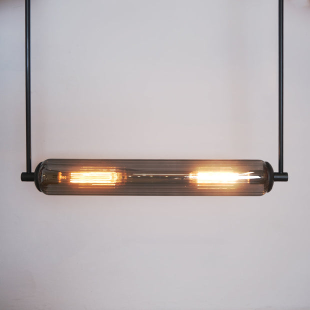 This modern lighting solution features an elongated glass tube encasing two glowing filament bulbs
