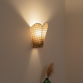 Wall-mounted lamp with checkered shade casting light on a plain wall.