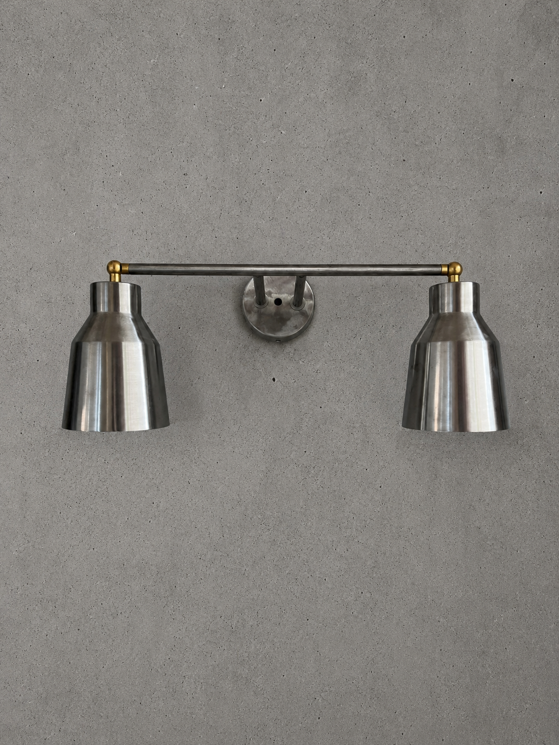 Wall-mounted lamp with two metallic shades on a gray wall