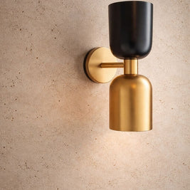 Wall-mounted light fixture with black top and gold base on a beige wall.
