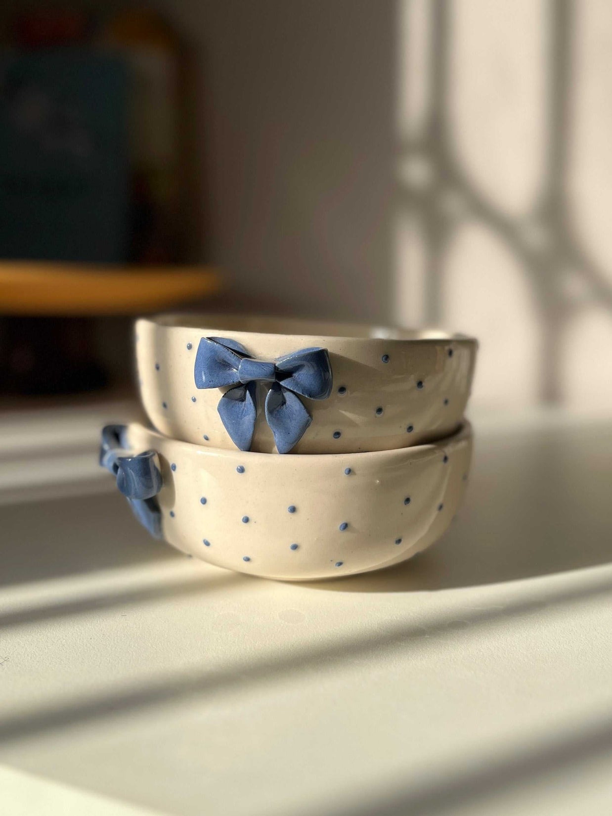 Two ceramic bowls with blue bow decorations on a light surface, with a blurred background.