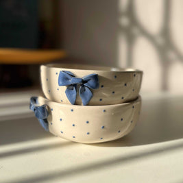 Two ceramic bowls with blue bow decorations on a light surface, with a blurred background.