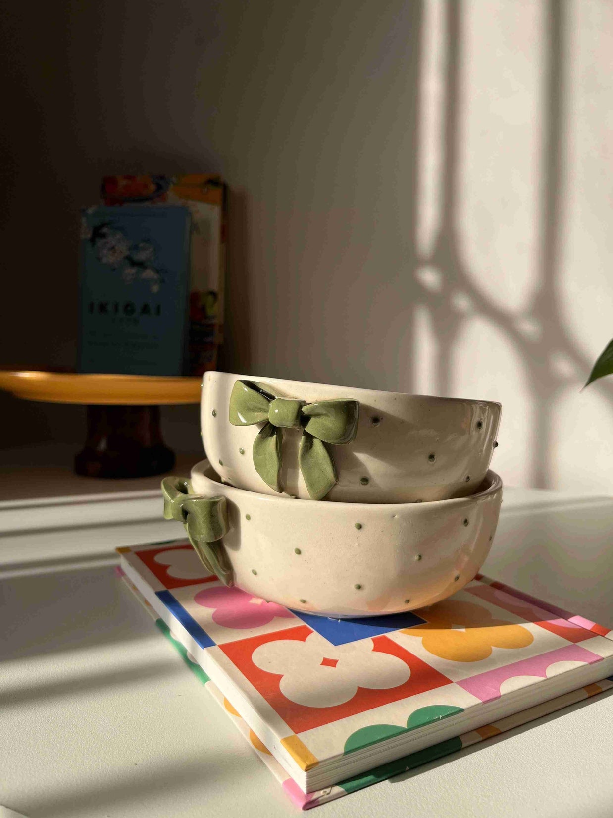 Dotted ceramic bowl with green bows on a shelf next to a colorful book