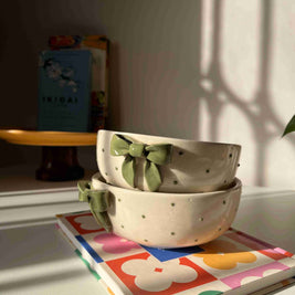 Dotted ceramic bowl with green bows on a shelf next to a colorful book