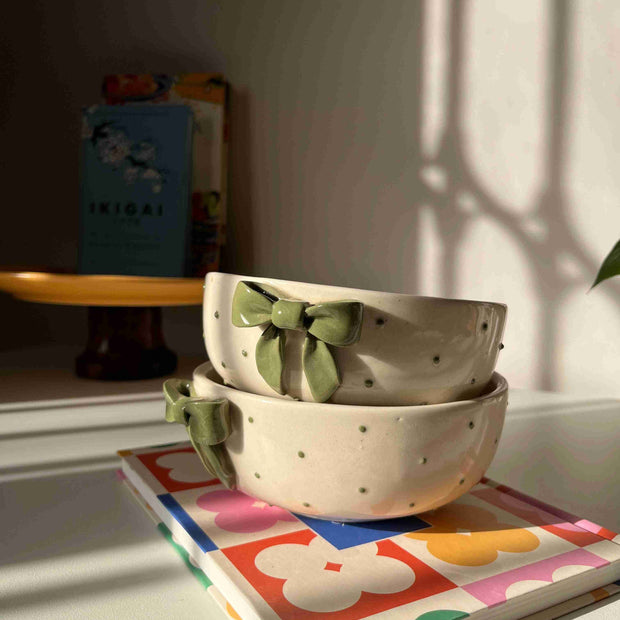 Dotted ceramic bowl with green bows on a shelf next to a colorful book