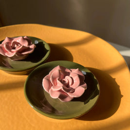 Two pink rose-shaped incense stick holders, placed on a warm yellow-orange surface with strong sunlight and shadows.