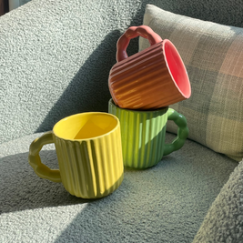 Three colourful fluted ceramic mugs styled together on a sofa chair