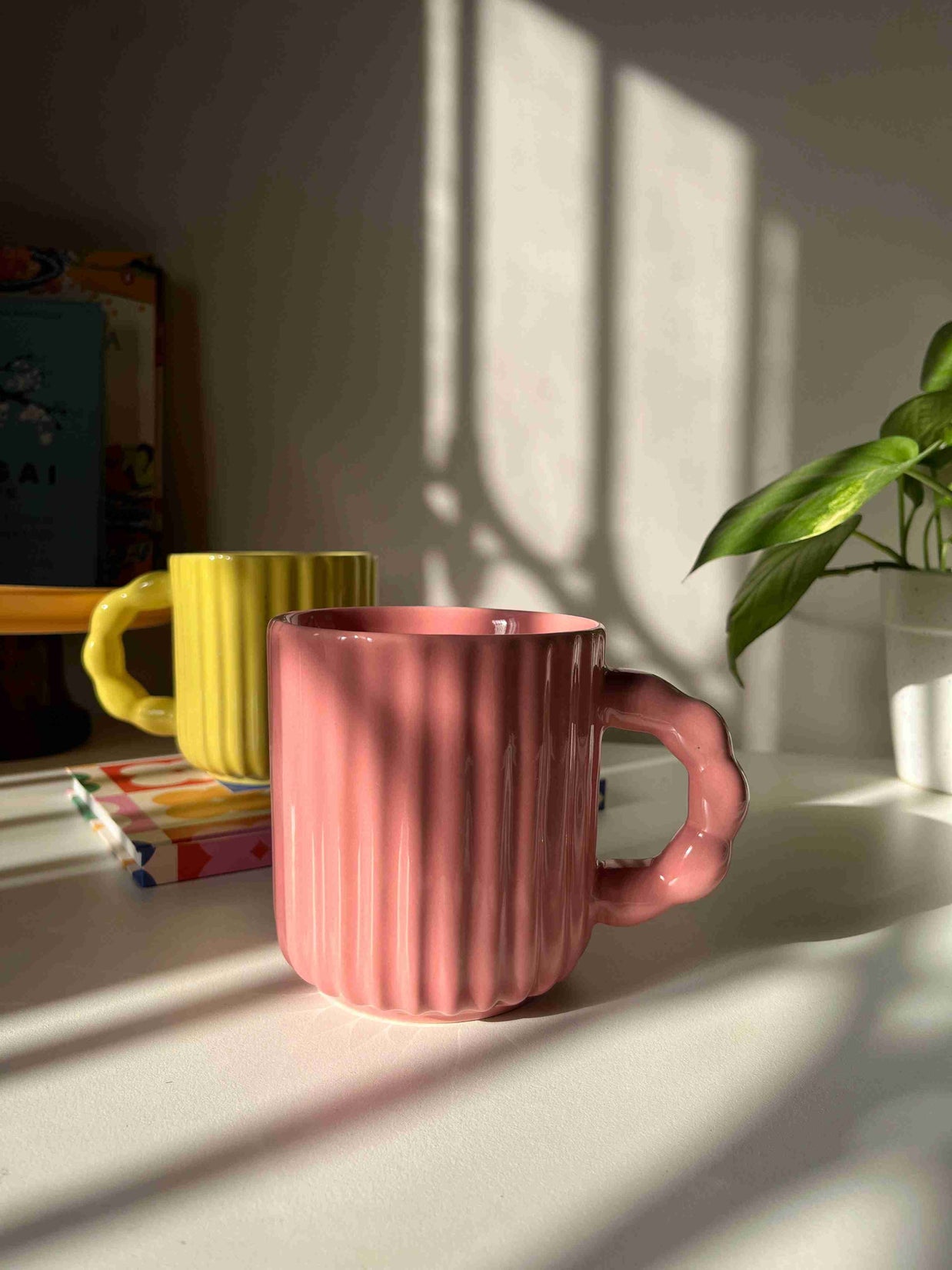 Pink ribbed mug on a white surface with shadows