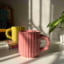 Pink ribbed mug on a white surface with shadows