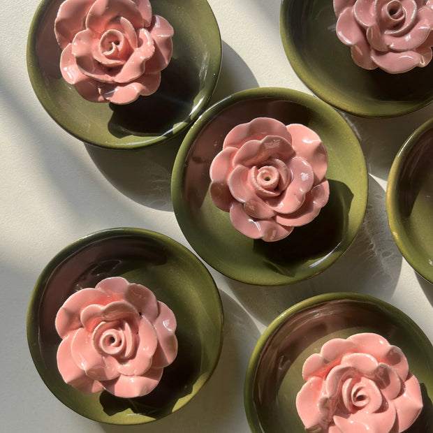 A close-up of pink flower detail on green ceramic incense holder, arranged on a light surface with strong natural shadows.