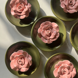 A close-up of pink flower detail on green ceramic incense holder, arranged on a light surface with strong natural shadows.