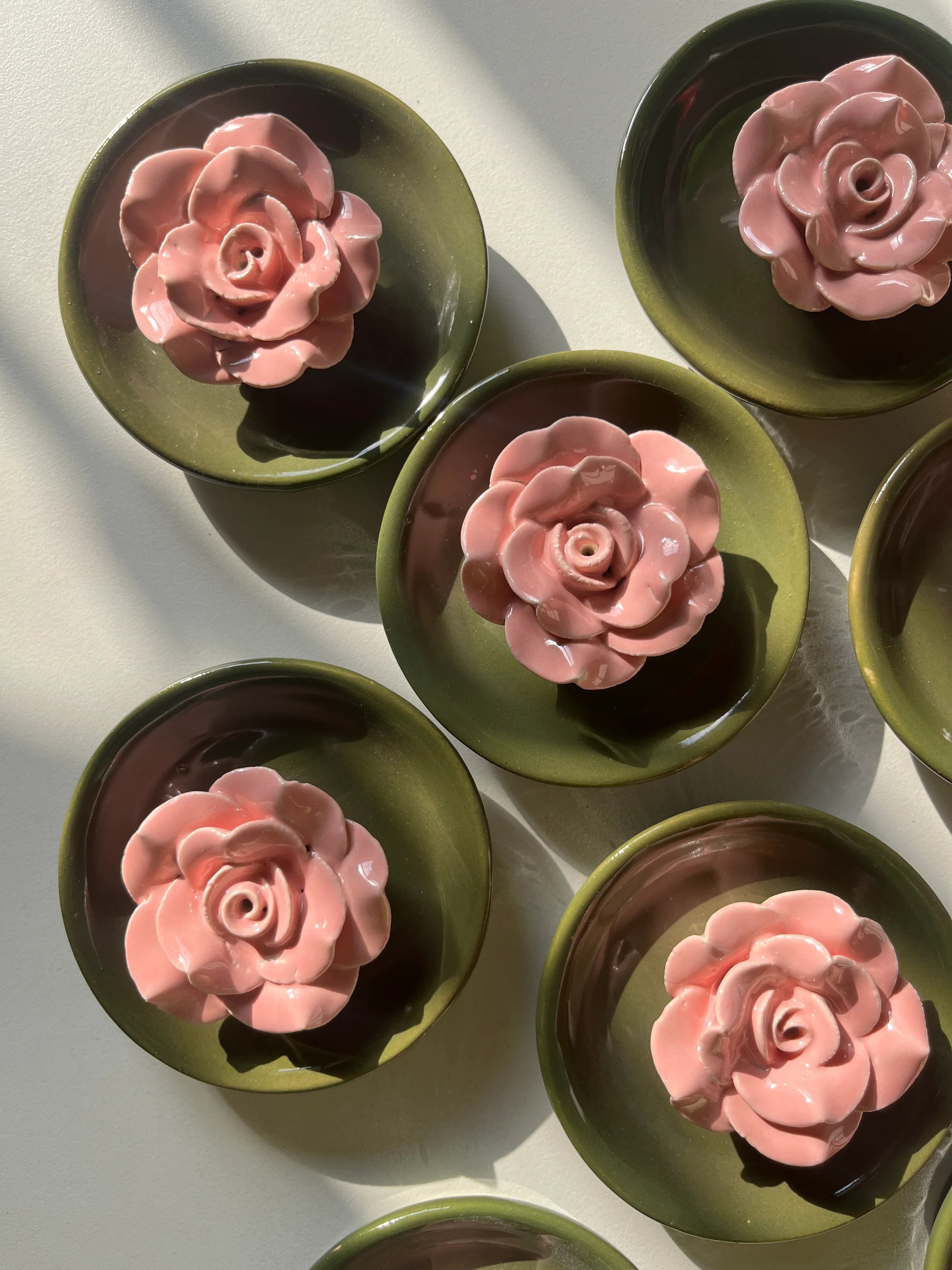 A close-up of pink flower detail on green ceramic incense holder, arranged on a light surface with strong natural shadows.