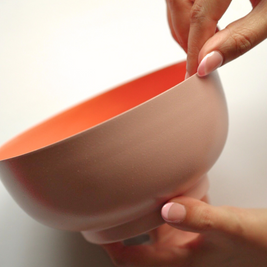 Person holding a pink and orange metal fruit salad bowl against a white background