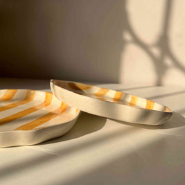 Modern striped yellow ceramic plates with a shadow on a neutral wall and white table