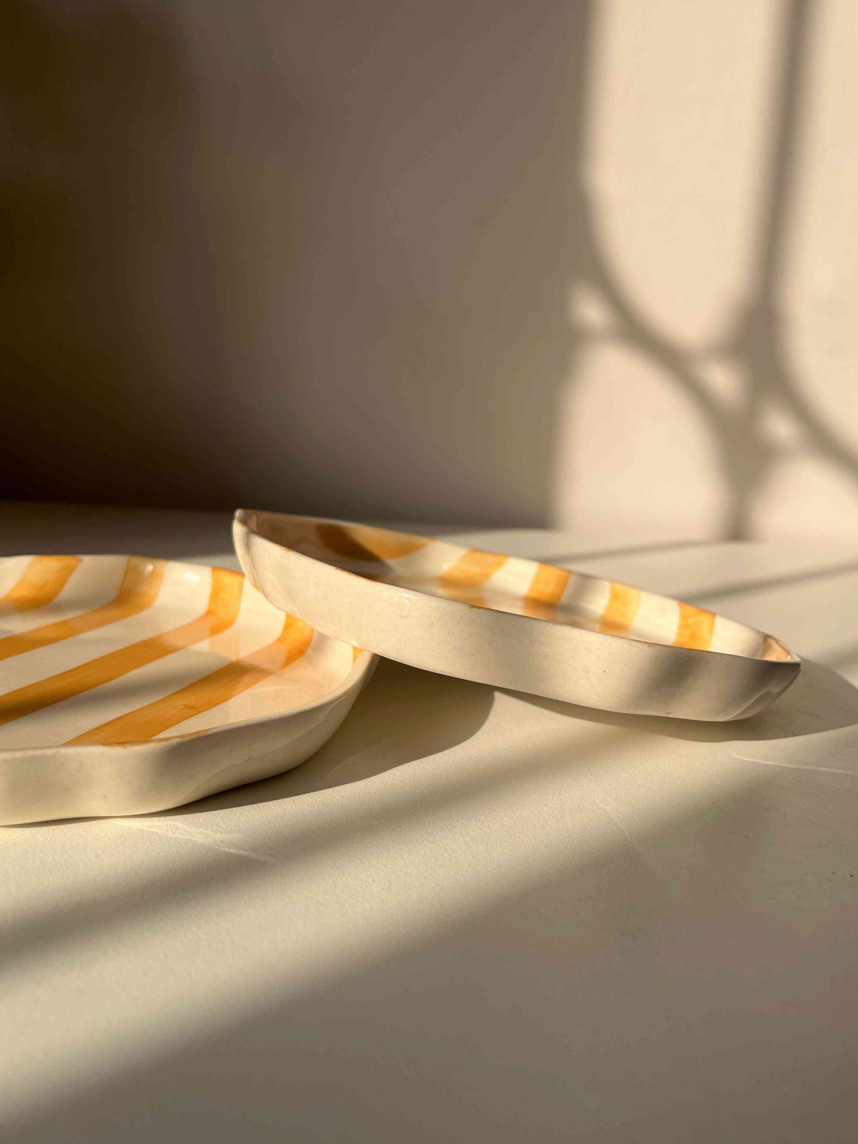 Modern striped yellow ceramic plates with a shadow on a neutral wall and white table
