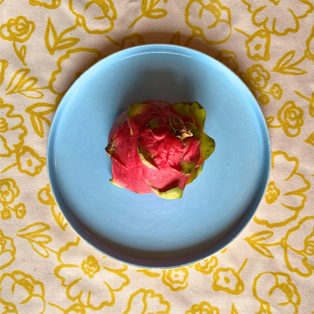 Cloud ceramic snack plate in pastel blue with a dragon fruit on a floral-patterned fabric background