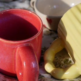 Red ember ceramic mug and yellow sunbeam madam jan mug on a floral-patterned surface